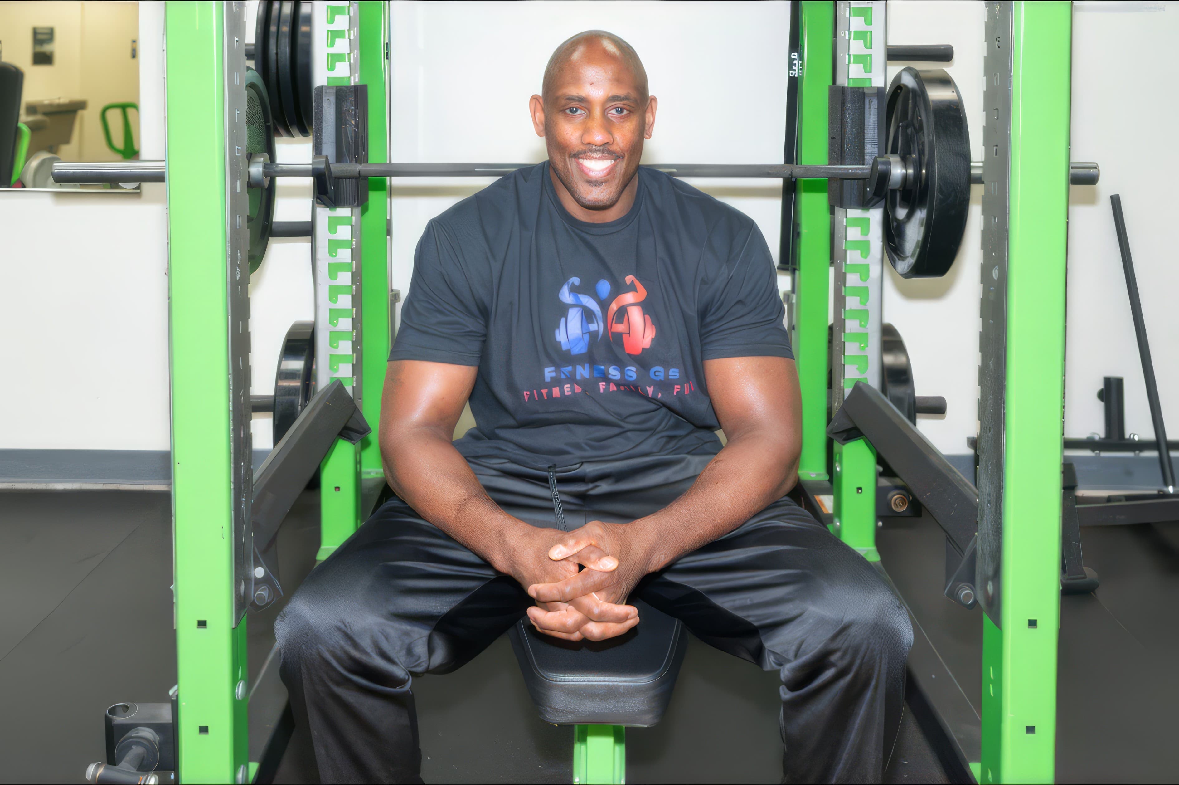 Coach Len sitting in his gym, smiling in a Fitness Gs shirt